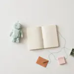 Flat-lay: small mint robot figurine beside an open notebook with a blue thread connecting to tiny pastel tool props, symbolizing an AI agent orchestrating narrow tools