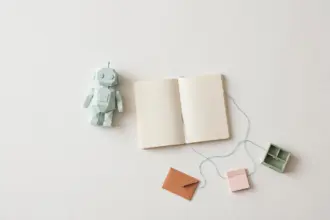 Flat-lay: small mint robot figurine beside an open notebook with a blue thread connecting to tiny pastel tool props, symbolizing an AI agent orchestrating narrow tools