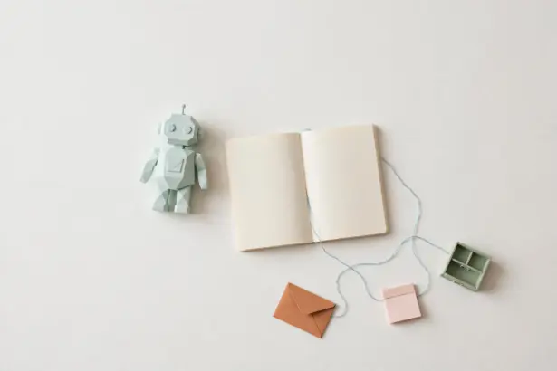 Flat-lay: small mint robot figurine beside an open notebook with a blue thread connecting to tiny pastel tool props, symbolizing an AI agent orchestrating narrow tools