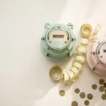 Flat-lay: two vintage-style utility meters side by side with a coiled measuring tape and brass coins, symbolizing double metering