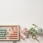 Flat-lay: pastel abacus with mint and peach beads beside three glass jars of pastel coins and a tiny magnifying glass, blush pink and sage palette