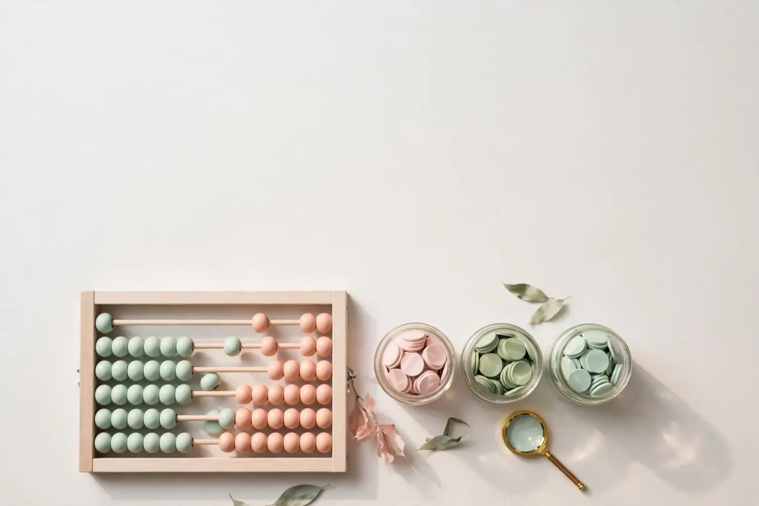 Flat-lay: pastel abacus with mint and peach beads beside three glass jars of pastel coins and a tiny magnifying glass, blush pink and sage palette