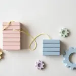 Flat-lay: two stacks of pastel wooden blocks, a tall blush pink beside a shorter powder blue, connected by pale yellow string, symbolizing the underdog challenger