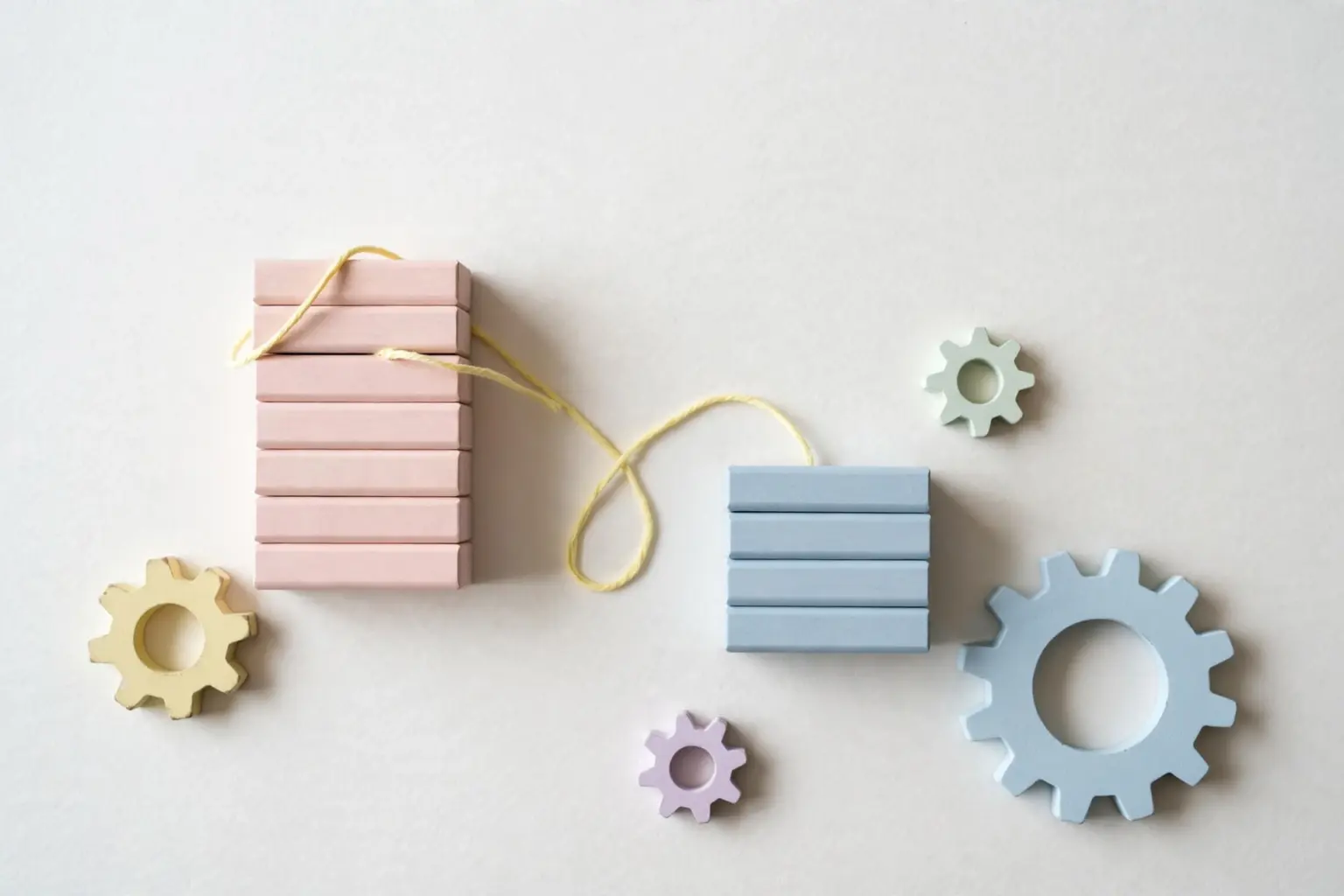 Flat-lay: two stacks of pastel wooden blocks, a tall blush pink beside a shorter powder blue, connected by pale yellow string, symbolizing the underdog challenger