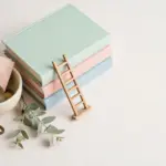 Flat-lay: small cream ceramic bowl with coins and a folded pastel banknote beside a miniature wooden ladder leaning on pastel books