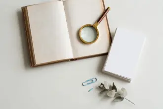 Flat-lay: open vintage hardcover book with a small magnifying glass resting on the page, a stack of white index cards beside it