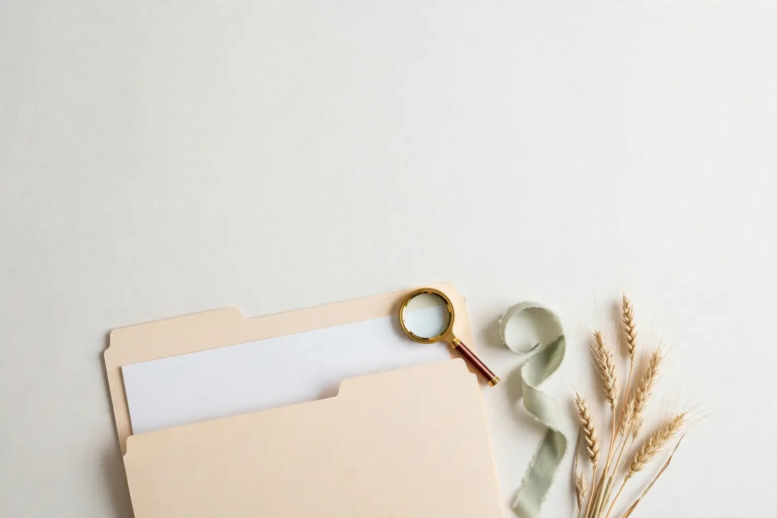 Flat-lay: open pastel beige manila folder with a document page, brass magnifying glass, sage ribbon and dried wheat