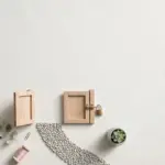 Flat-lay: two small wooden garden gates on a pale off-white background, one open and one closed with a tiny brass padlock, a curved pebble path between them and a small potted succulent beside