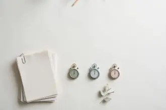 Flat-lay: a neat stack of blank paper reports beside a row of three small pastel stopwatches in mint, blue and pink on a pale off-white background