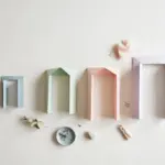 Flat-lay: four pastel paper doorway frames in blue, mint, peach and lavender growing taller in a row on a pale off-white background, with small clips and a eucalyptus sprig scattered below