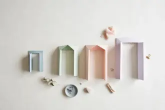 Flat-lay: four pastel paper doorway frames in blue, mint, peach and lavender growing taller in a row on a pale off-white background, with small clips and a eucalyptus sprig scattered below