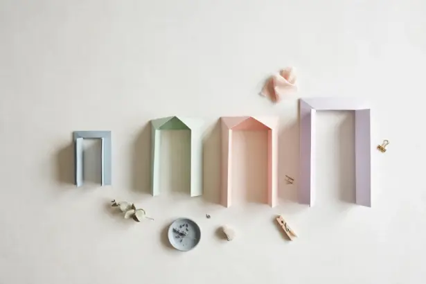 Flat-lay: four pastel paper doorway frames in blue, mint, peach and lavender growing taller in a row on a pale off-white background, with small clips and a eucalyptus sprig scattered below