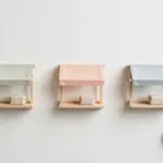 Flat-lay: three miniature market stalls in pastel canvas and wood standing in a row on a pale off-white background, each with one small blank paper parcel on its counter
