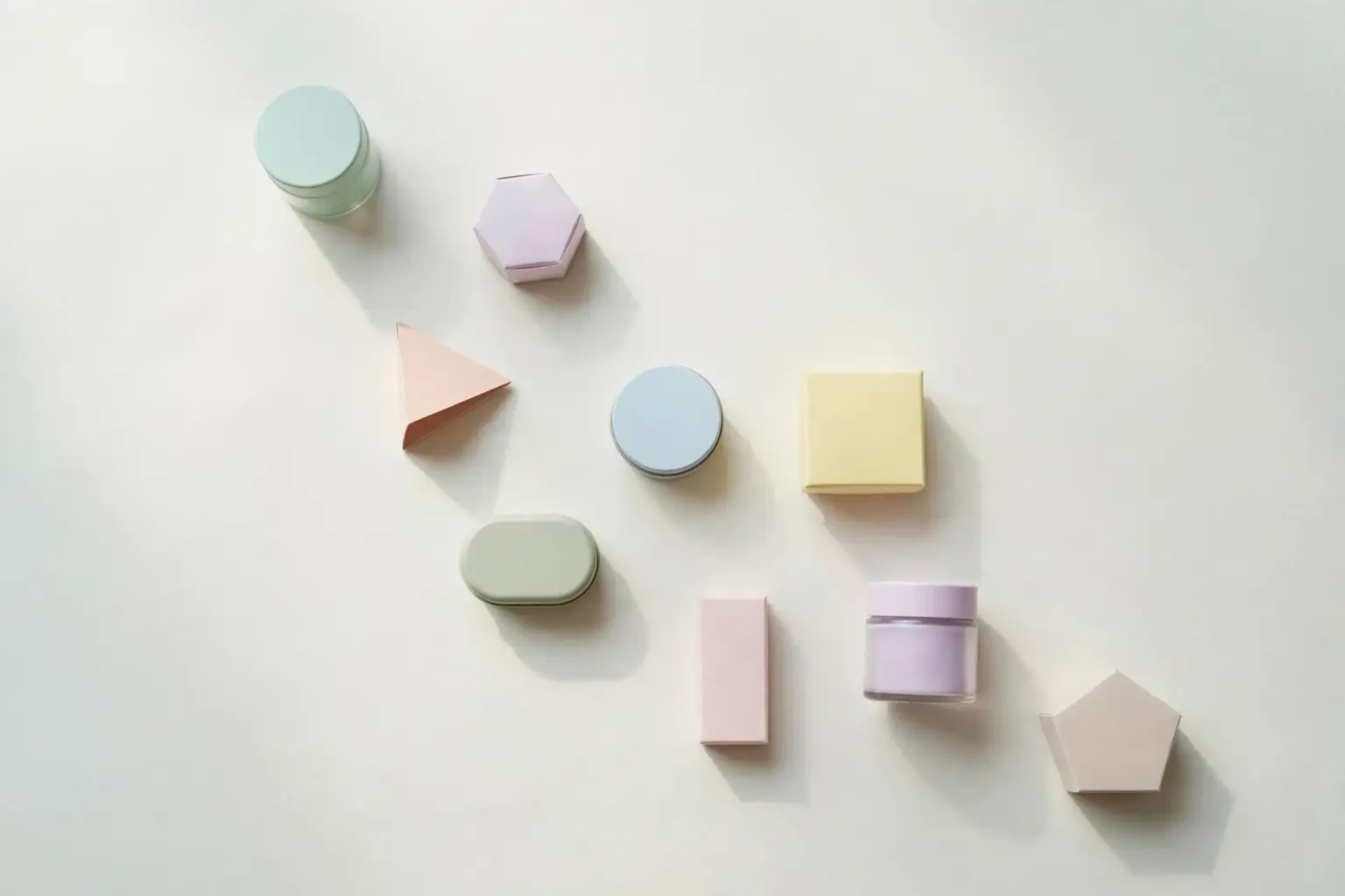 Flat-lay: a small market stall shelf holding nine tiny pastel jars and boxes of different shapes in a row on a pale off-white background