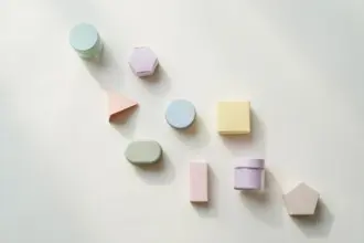 Flat-lay: a small market stall shelf holding nine tiny pastel jars and boxes of different shapes in a row on a pale off-white background