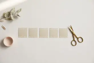 Flat-lay: one long ribbon of pale film strip cut into several neat short segments laid in a row, with small brass scissors resting beside them on a pale off-white background